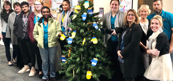 a crowd of Phi Theta Kappans standing surrounding a pine tree with paper mittens adorning it.